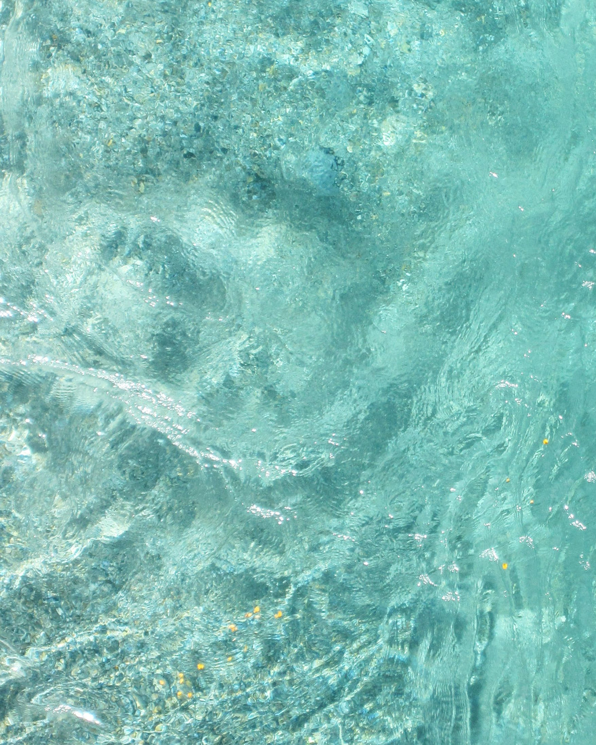 A full-frame close-up of turquoise sea water with ripples, light reflections, and subtle speckling.