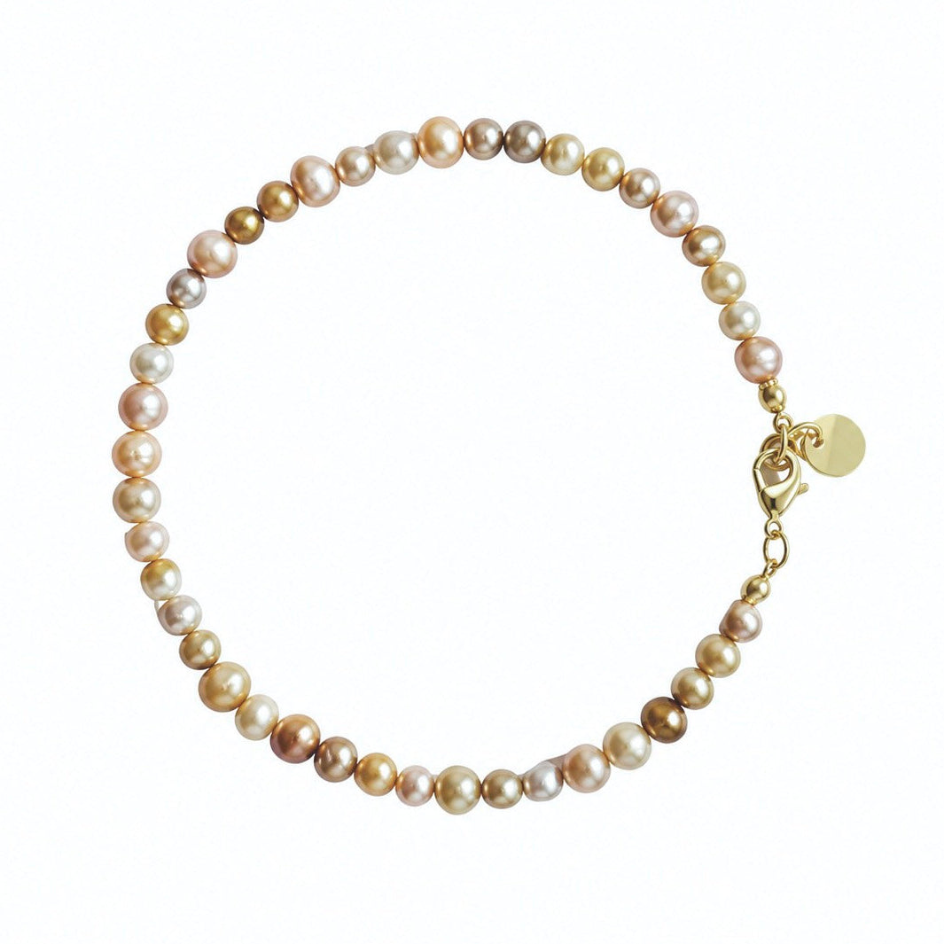A strand of irregular freshwater pearls in shades of cream, beige, and light brown, threaded with a gold clasp and a small round gold tag, shown on a plain white background.