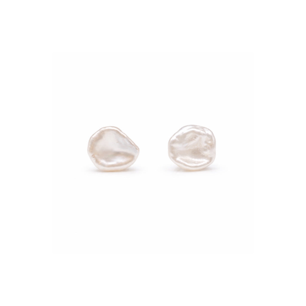 A pair of irregular-shaped organic white pearl stud earrings shown on a plain white background