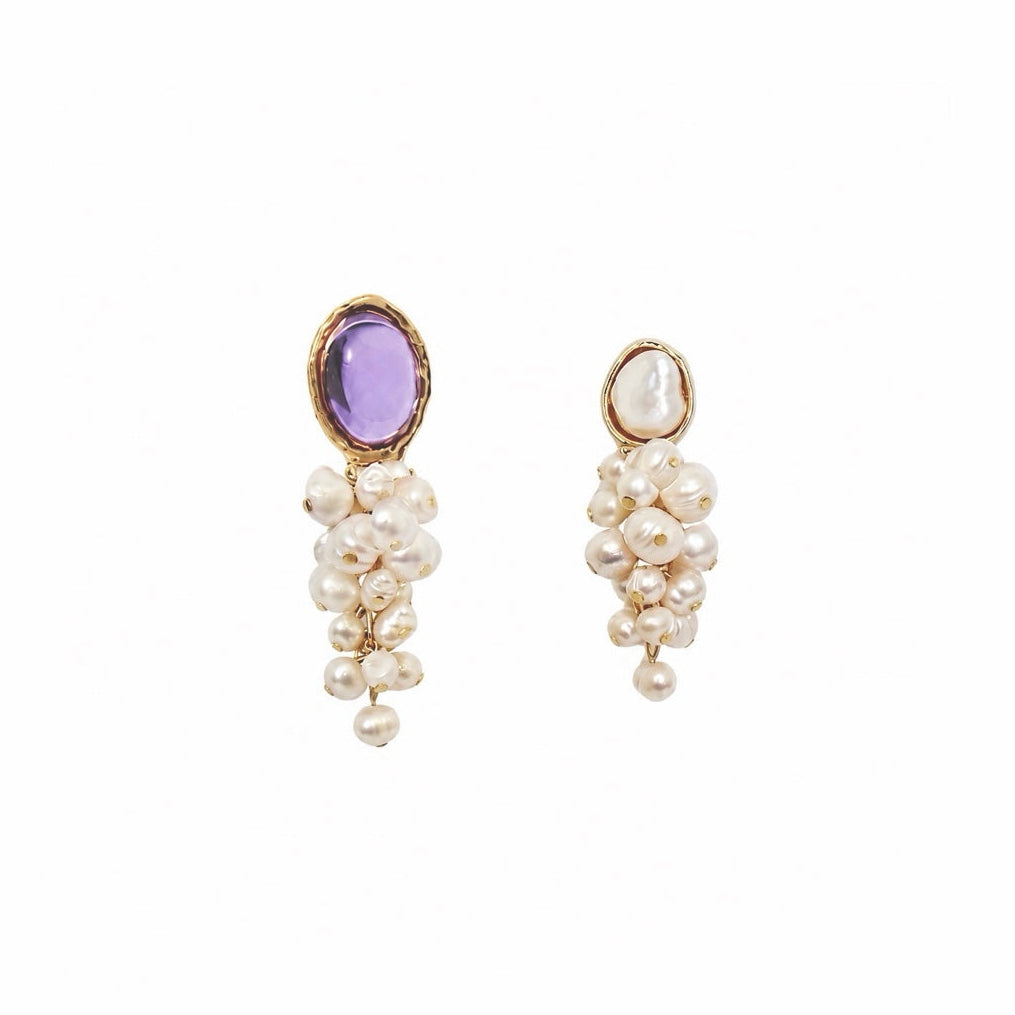 A pair of gold drop earrings featuring a round purple amethyst stone at the top and a cascading cluster of baroque pearls below, set against a plain white background.