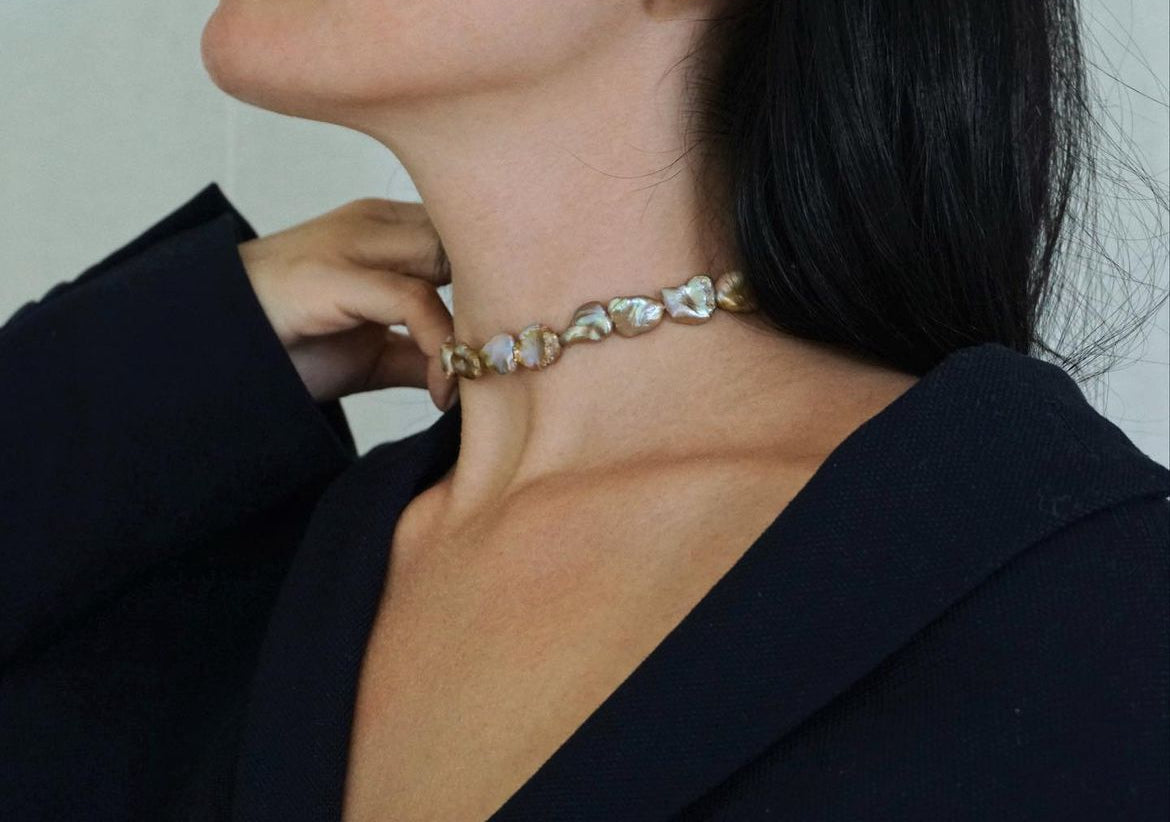A close up shot of a woman wearing a necklace made of pearls with organic irregular shapes and tone of gold champaign.