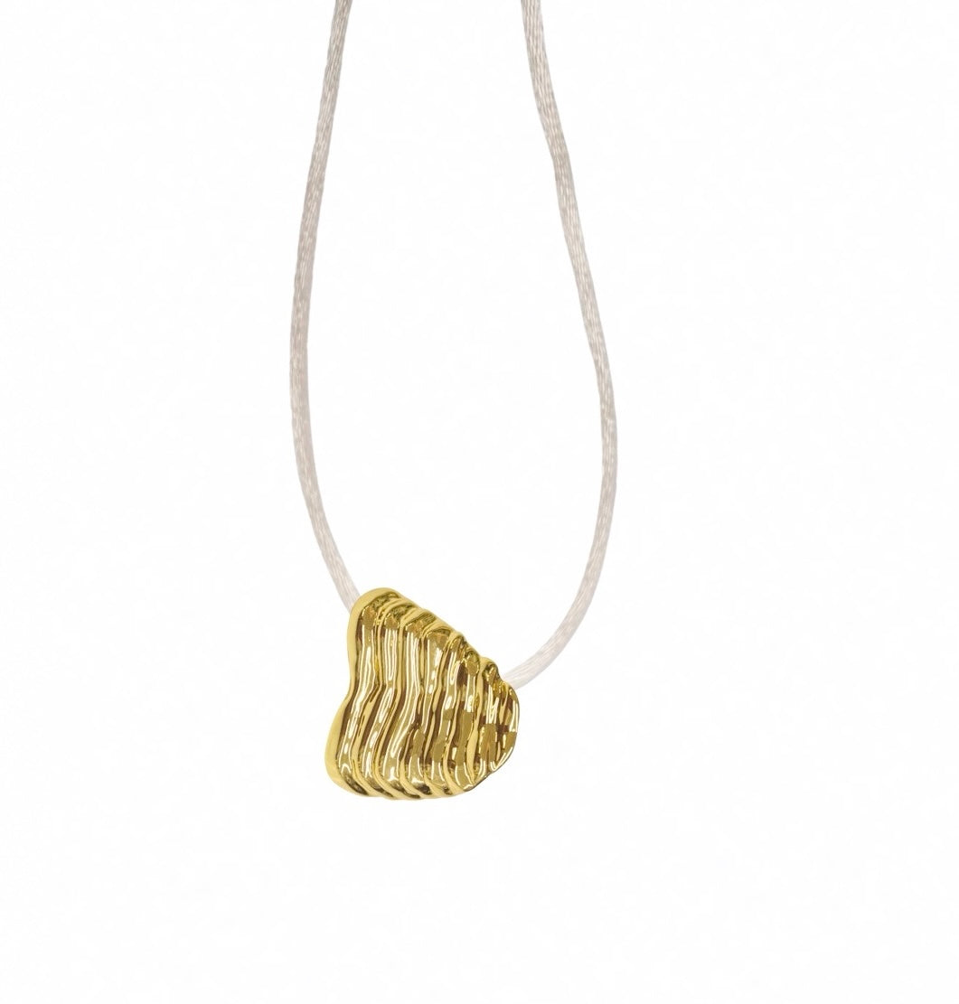 A gold wave-shaped pendant with a wavy, layered design, suspended from a thin off-white cord against a solid white background.
