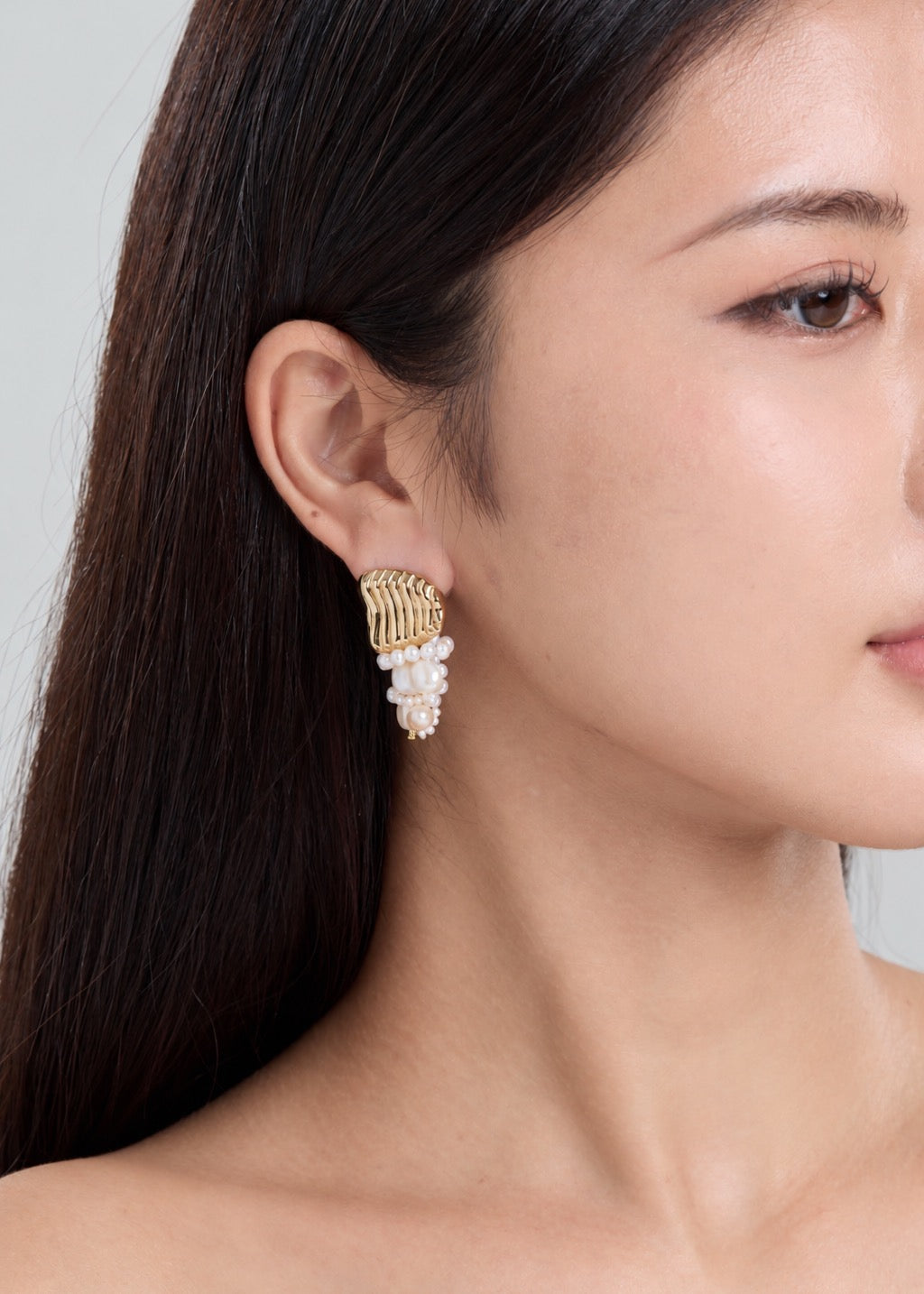 A close-up side profile of a woman wearing a gold and white pearl dangle earring.