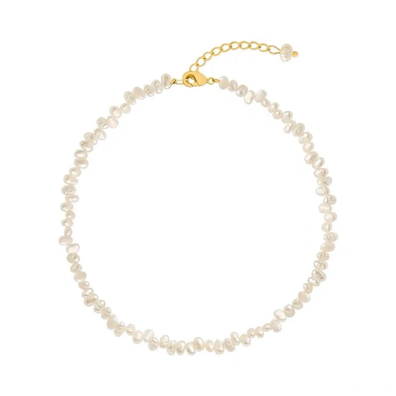 A delicate necklace made of small irregular white pearls on a gold-tone chain with a lobster clasp and extender, shown on a plain white background.