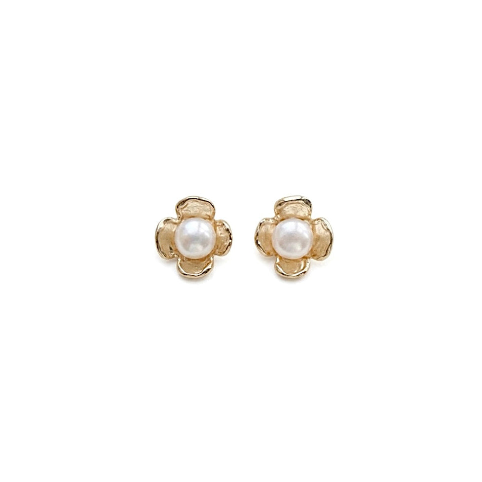 A pair of stud earrings with gold flower shape with a round white pearl in the center, shown on a plain white background