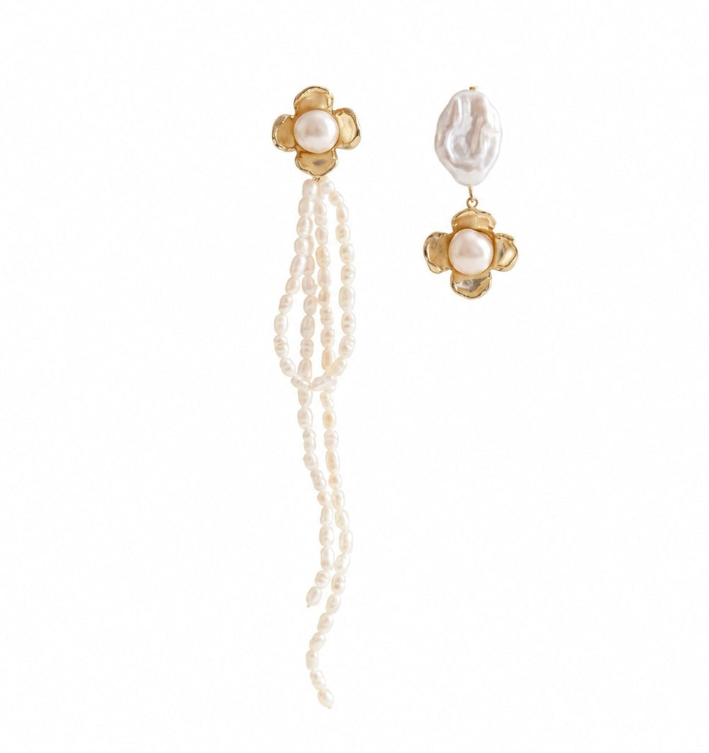 A pair of gold and pearl drop earrings on a plain white background. One earring features a gold flower-shaped stud with a pearl and a long dangling strand of small white pearls.