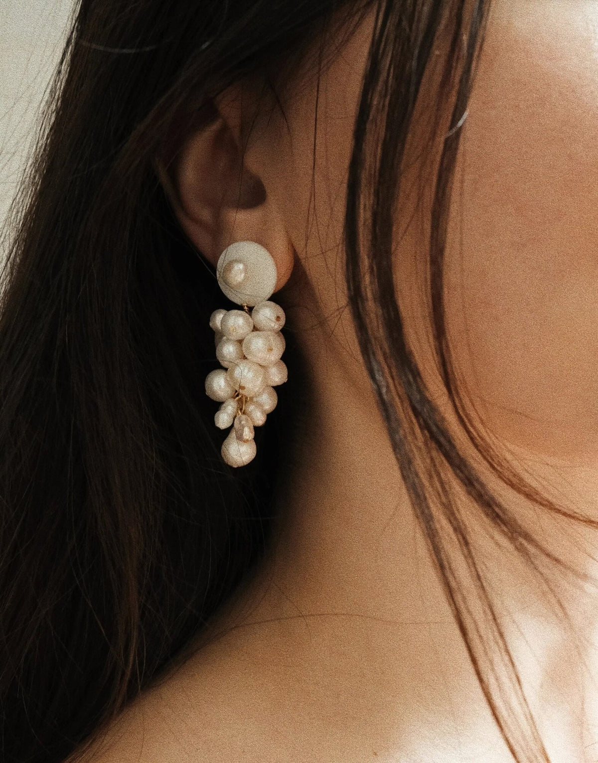 A close-up of a model's ear wearing a dangling pearl cluster earring with a round white top stud.