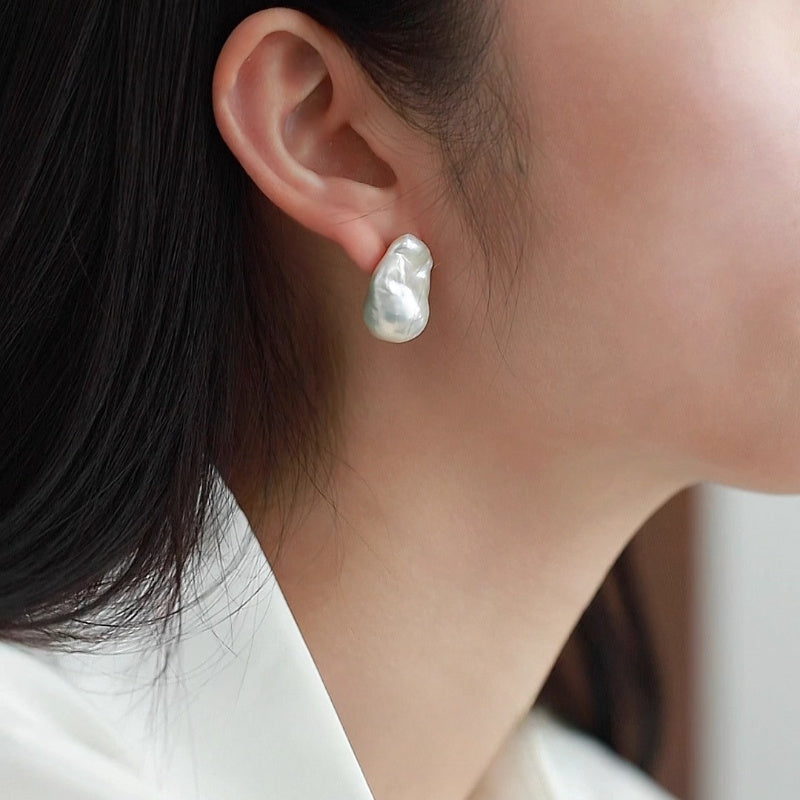 A close-up of a person's ear wearing a single irregular, organic-shaped white pearl stud earring.