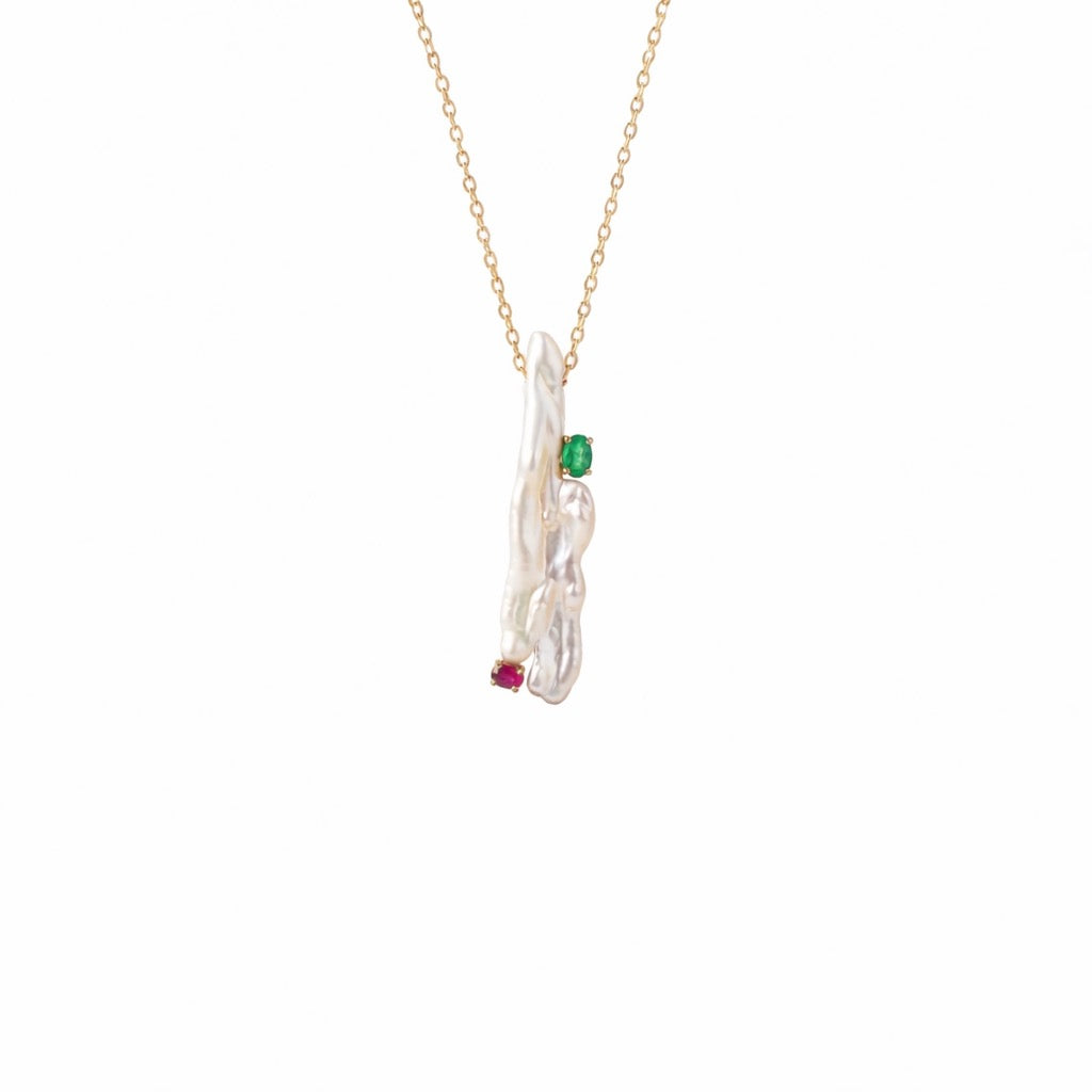 A delicate gold chain necklace featuring an abstract, organic-shaped pendant made of white pearl, accented with a small green gemstone and a tiny red gemstone, shown against a plain white background.