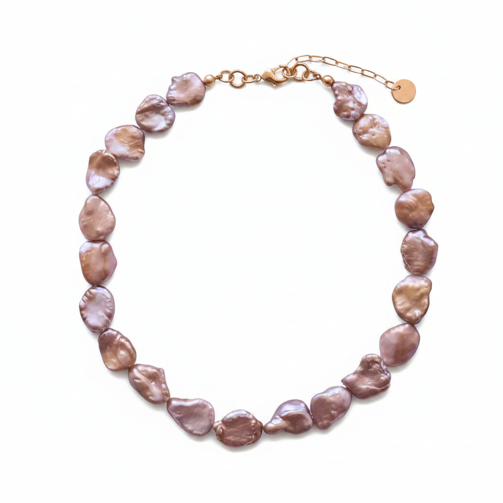 A baroque pearl necklace with irregular, organic-shaped pearls in shades of champagne and purple, accented by a gold-tone chain clasp and extender.
