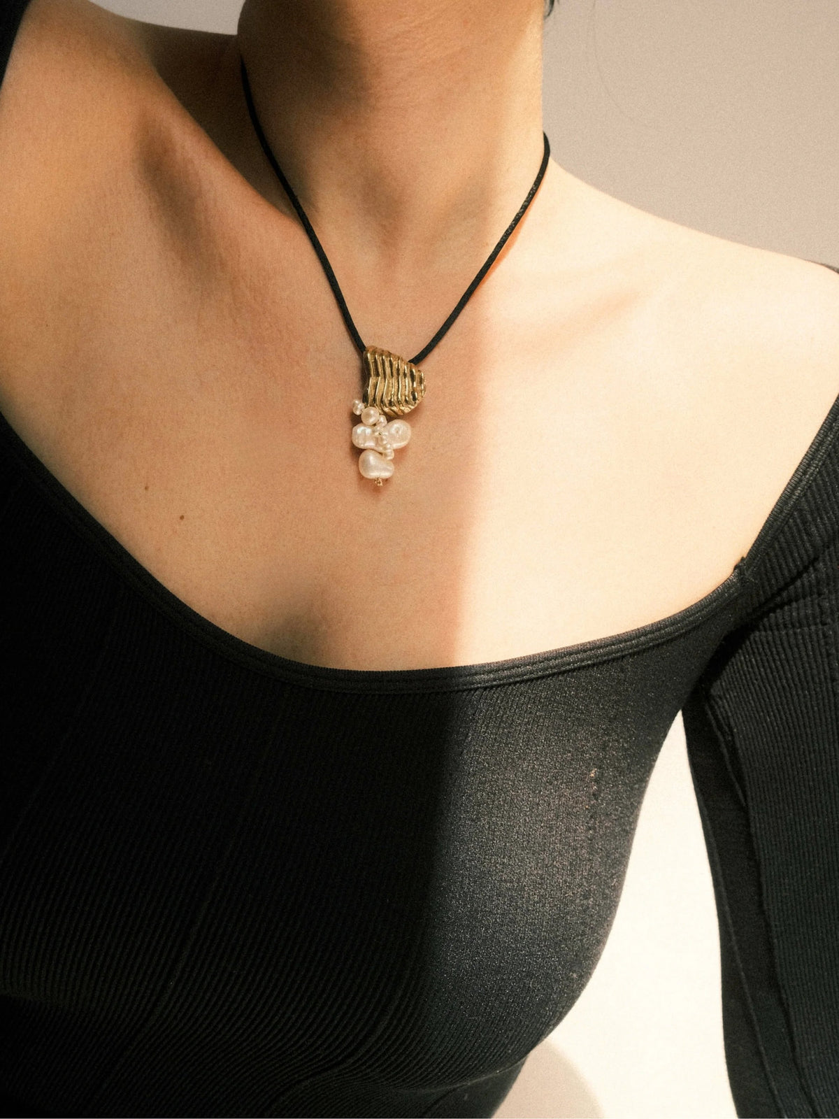 Necklace with a golden pendant worn by a person against a neutral background