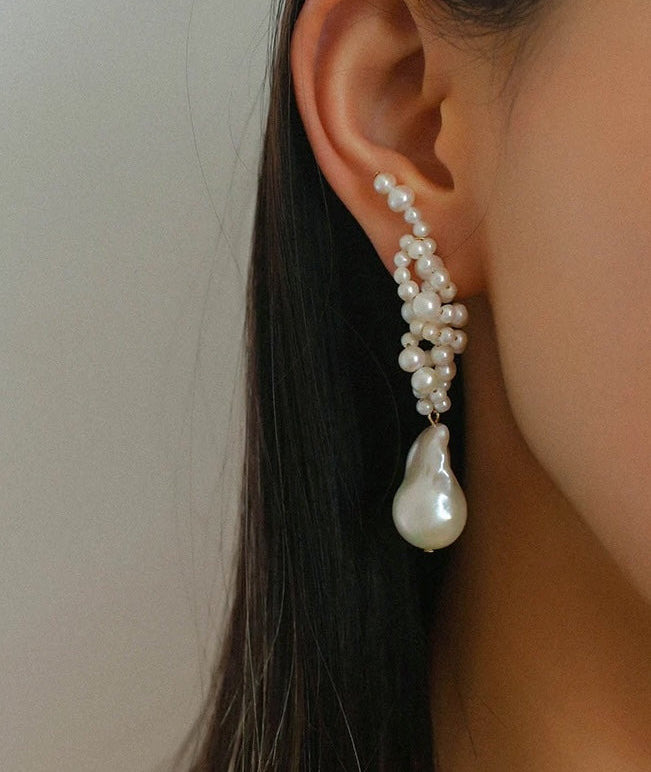 A close-up of a person's ear wearing a long, multi-strand pearl dangle earring with a large teardrop-shaped pearl drop.